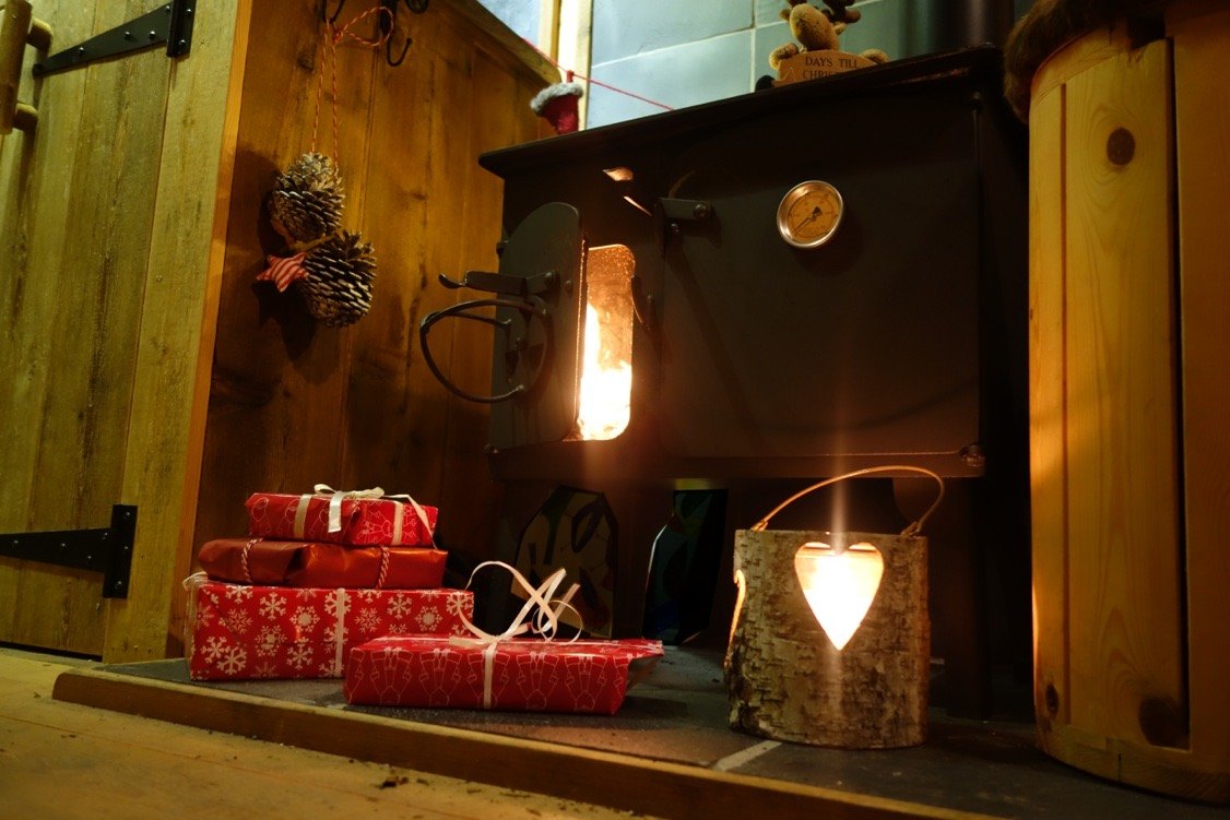 Wrapped Christmas presents and a glowing lantern on the hearth beside the log burner